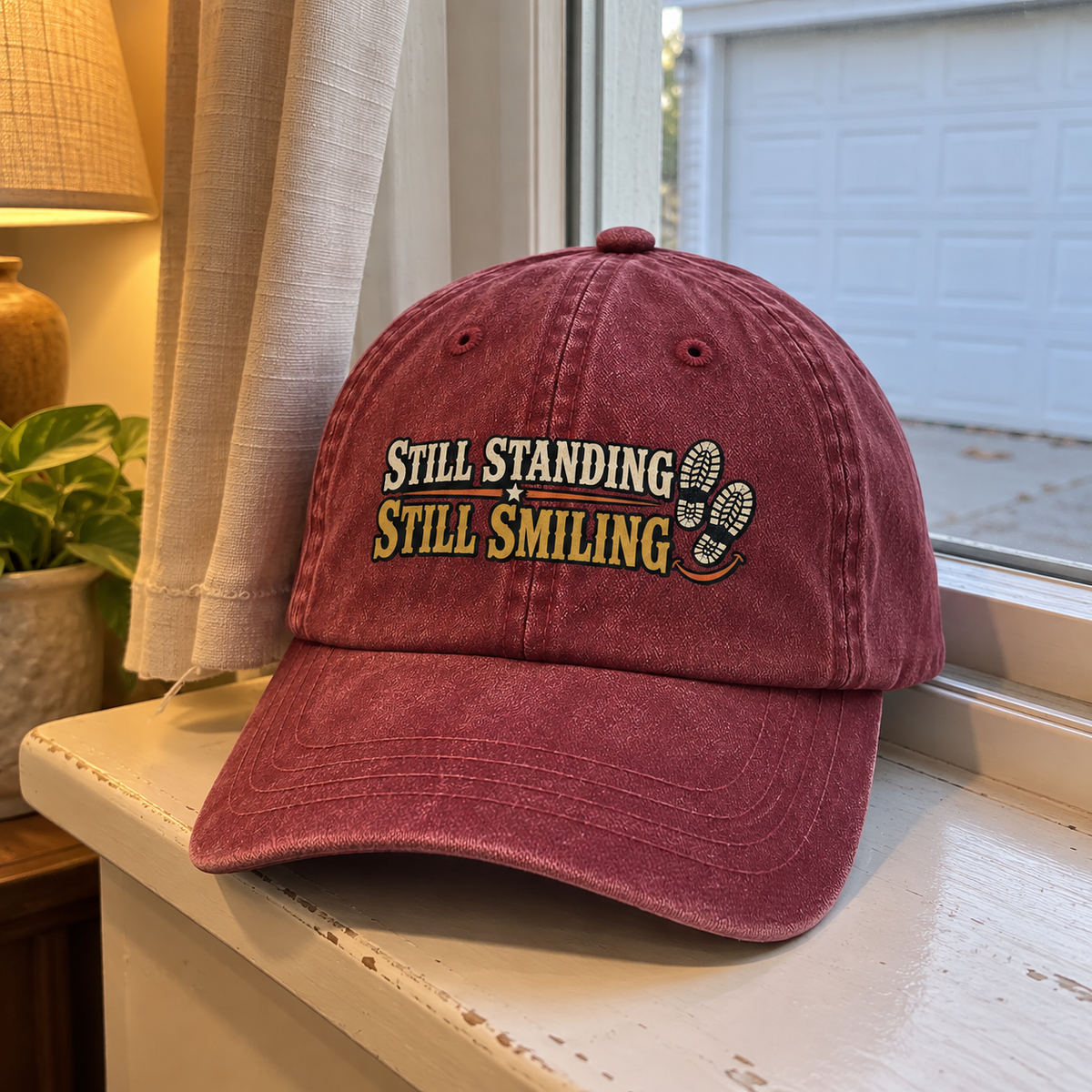 Burgundy vintage washed cap with printed Still Standing Still Smiling slogan on windowsill
