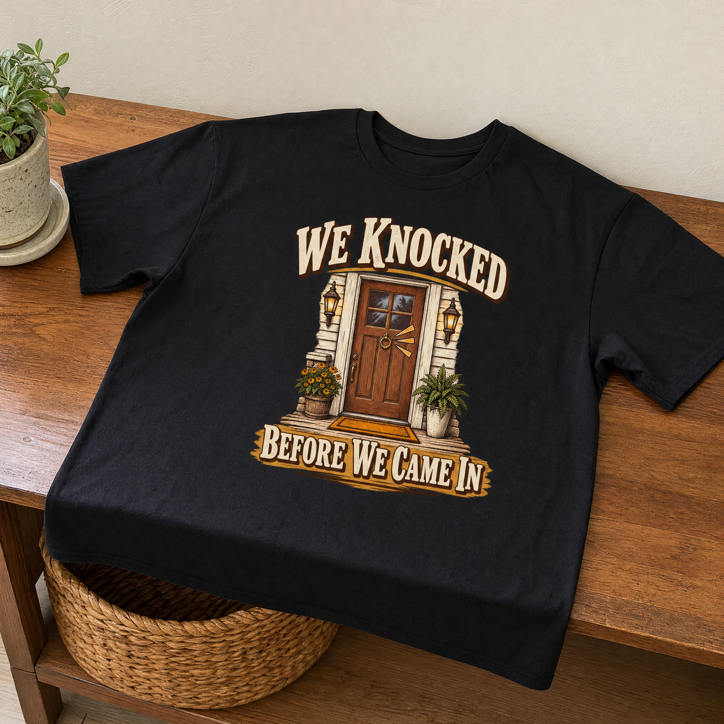 Black vintage t-shirt with printed We Knocked Before We Came In design on wooden table