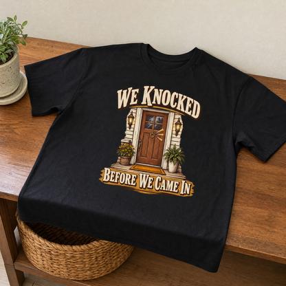 Black vintage t-shirt with printed We Knocked Before We Came In design on wooden table