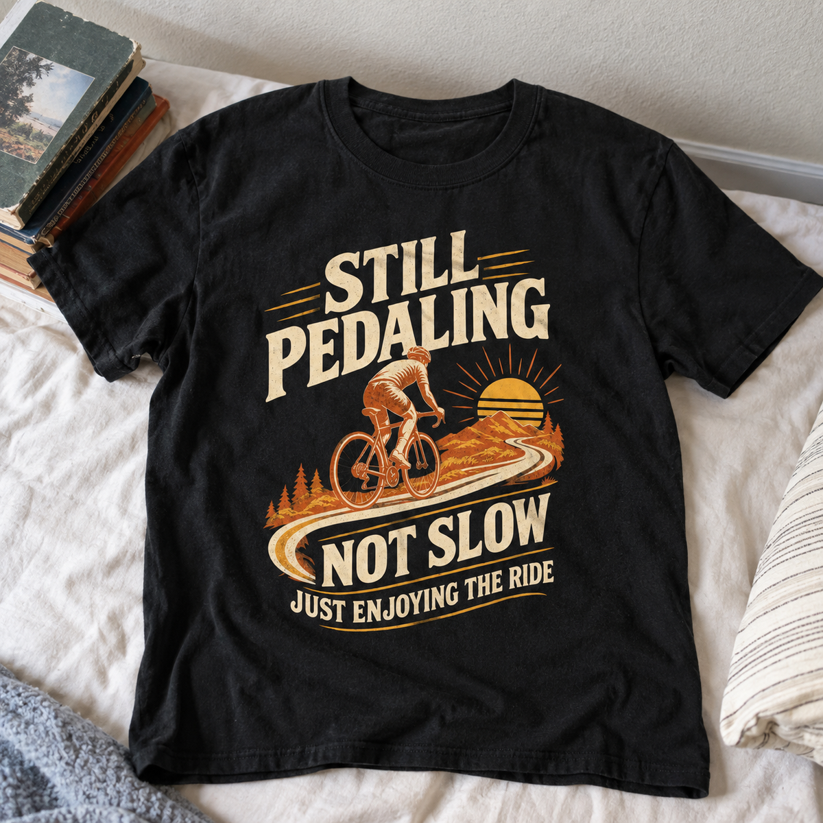 Black vintage t-shirt with printed Still Pedaling cycling slogan and mountain sunset graphic, top view