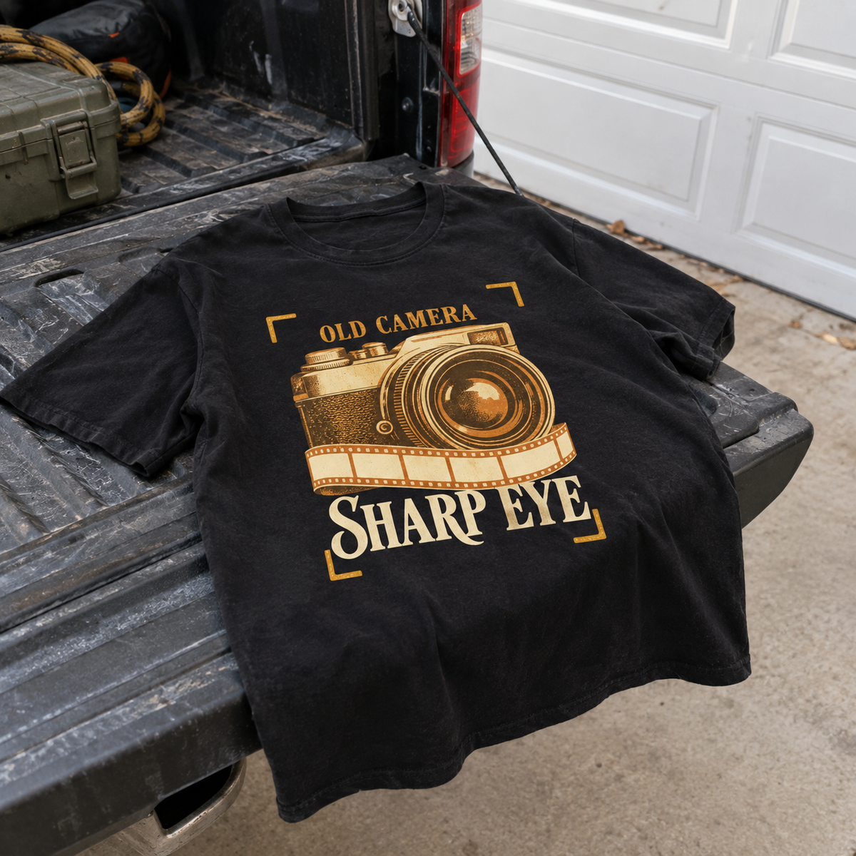 Black vintage T-shirt with printed old camera and Sharp Eye slogan, hero view on truck bed