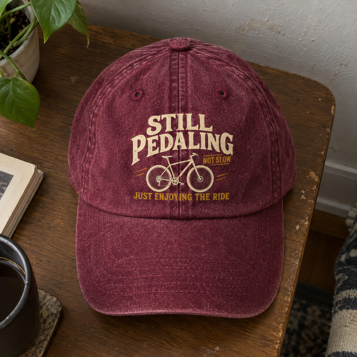 Burgundy vintage washed cap with printed bicycle bicycle design and Still Pedaling slogan, front hero view