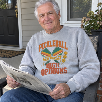 Gray vintage sweatshirt with printed pickleball design and slogan worn by senior man reading newspaper on porch
