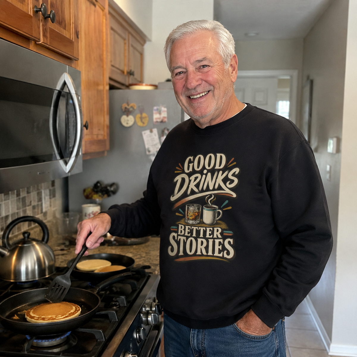 Senior man wearing black vintage sweatshirt with printed Good Drinks Better Stories design in kitchen