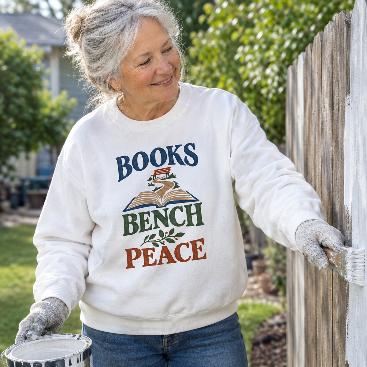 White vintage sweatshirt with Books Bench Peace print, worn by senior woman painting a fence outdoors