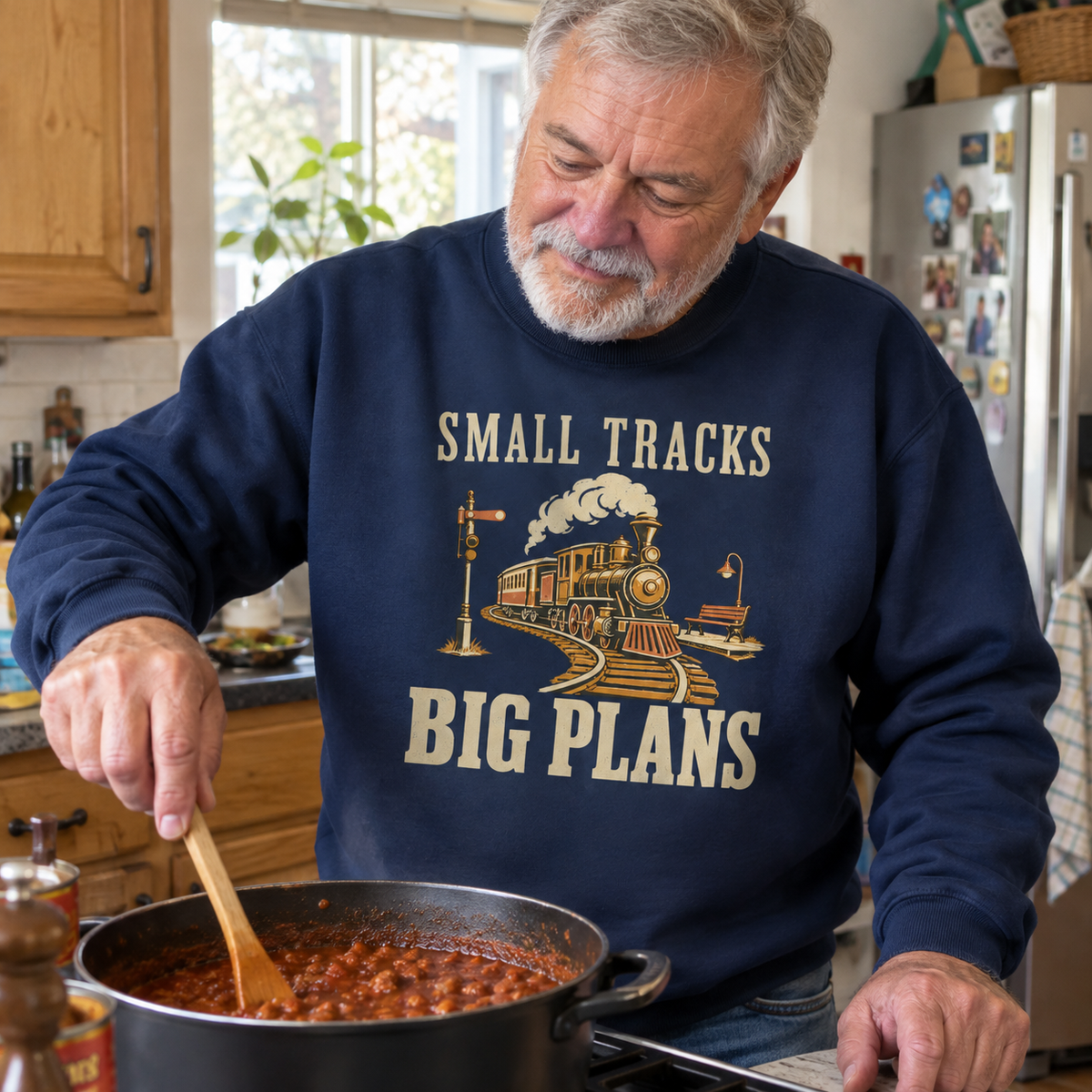 Senior man in navy vintage sweatshirt with printed Small Tracks Big Plans train design, cooking