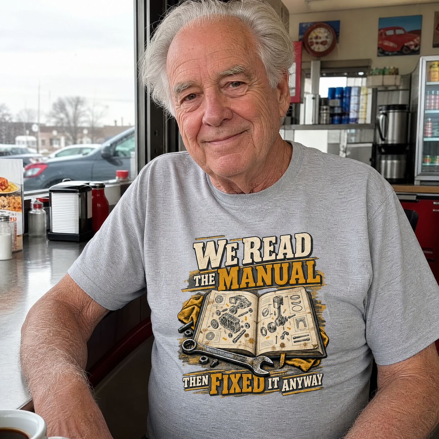Senior man wearing gray vintage t-shirt with printed manual repair slogan, seated in diner.