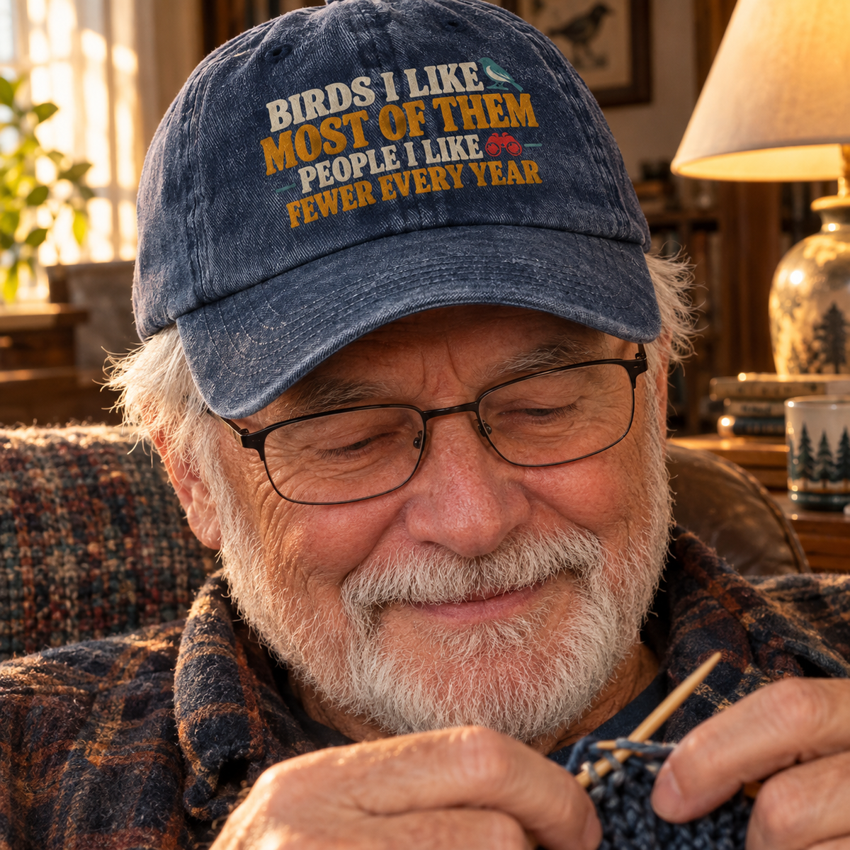 Vintage washed cap with printed bird slogan worn by senior man knitting indoors, close-up view