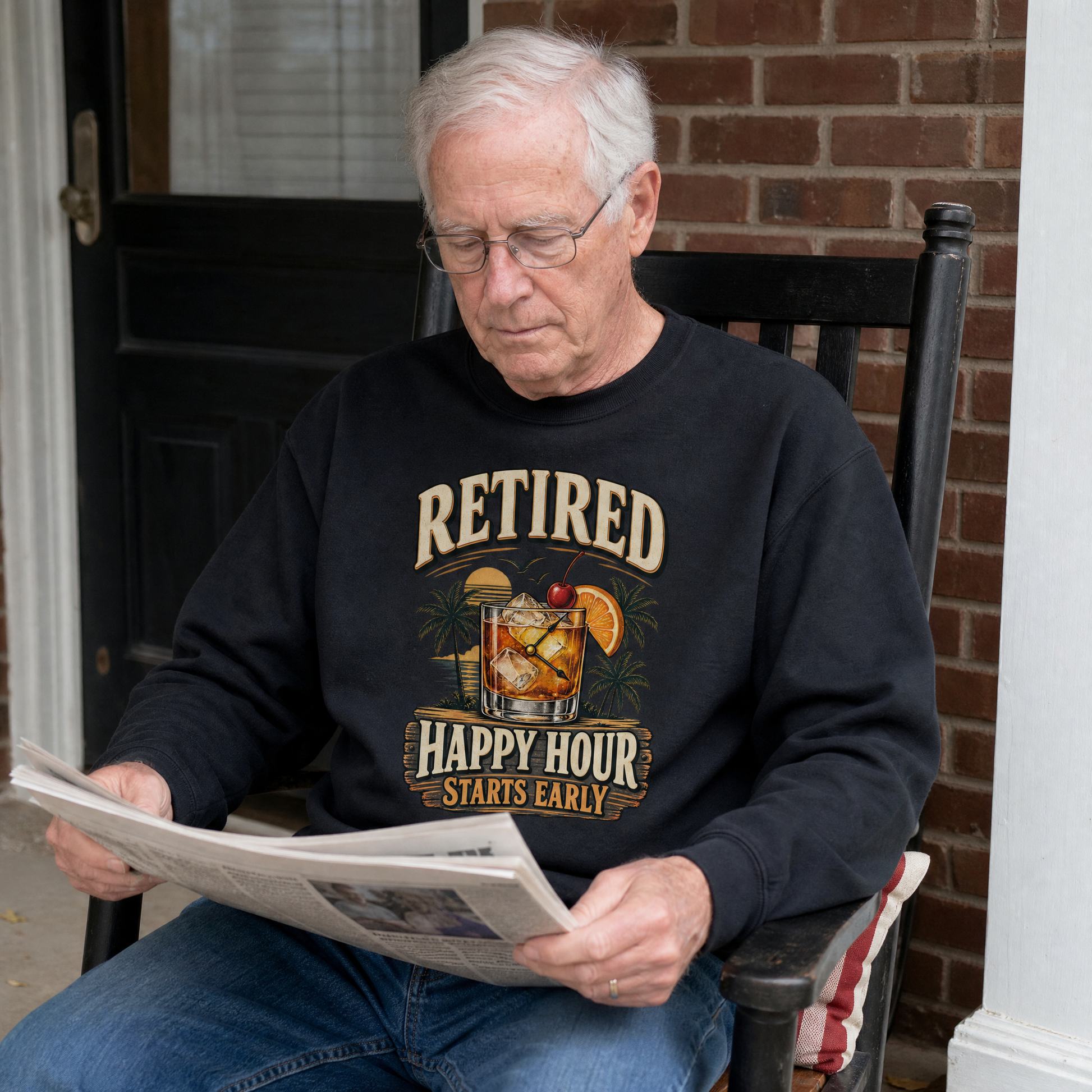 Black vintage sweatshirt with printed “Retired Happy Hour Starts Early” worn by senior man outdoors.
