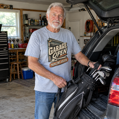 Gray vintage t-shirt featuring printed “Garage Open Problems Solved” worn by senior man in garage.