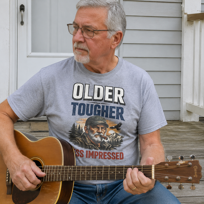 Senior man wearing gray vintage t-shirt with printed Older Tougher Less Impressed slogan playing guitar