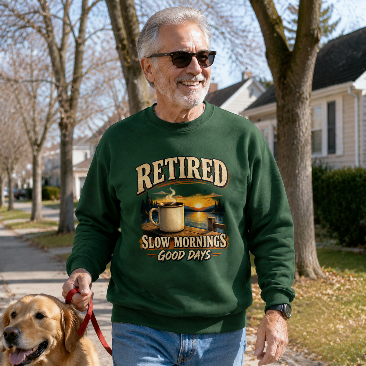 Senior man wearing green vintage sweatshirt with printed “Retired Slow Mornings Good Days” design walking dog.