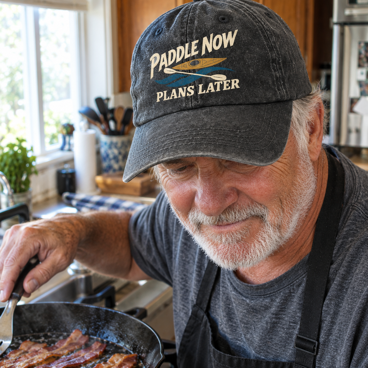 Black vintage washed cap with printed Paddle Now Plans Later slogan on senior man cooking