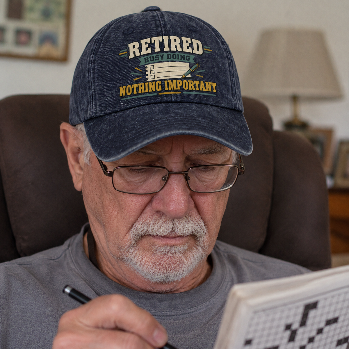 Senior man wearing a navy vintage washed cap with printed retirement slogan, seated indoors.