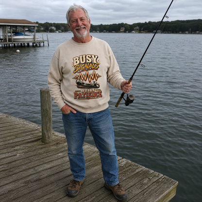 Senior man wearing beige vintage sweatshirt reading Busy Signals Built Patience, fishing by lakeside dock.