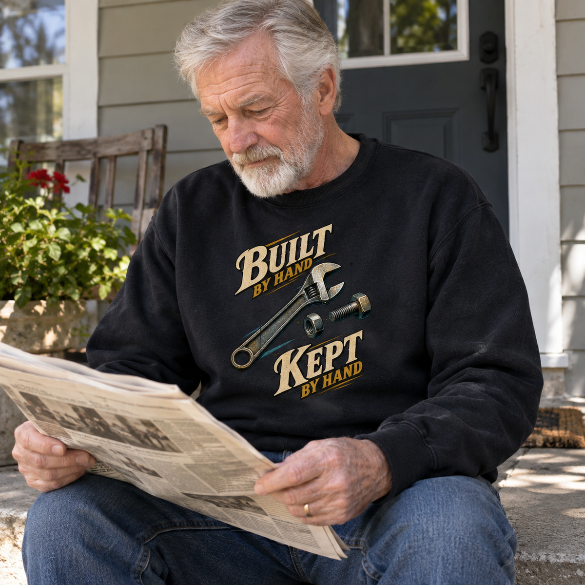 Black vintage sweatshirt with printed Build By Hand slogan, worn by senior man reading newspaper.