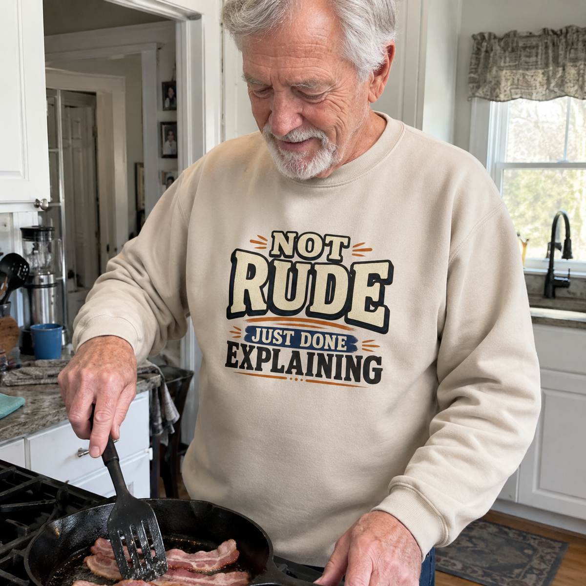Senior man wearing a beige vintage sweatshirt with printed Not Rude slogan while cooking in kitchen