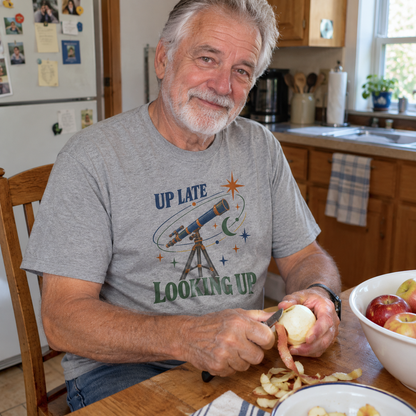 Senior man wearing gray vintage t-shirt with printed Up Late Looking Up design in kitchen