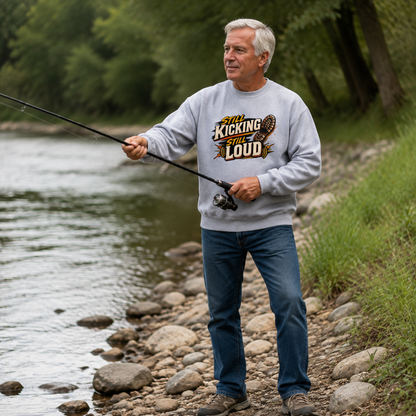 Gray vintage sweatshirt with printed “Still Kicking Still Loud” slogan worn by senior man fishing by river.