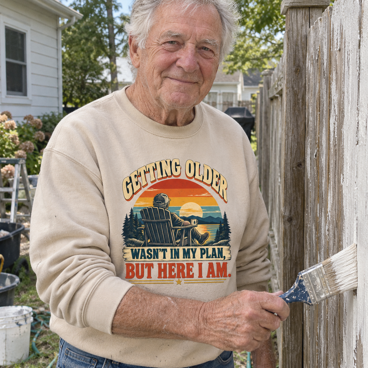 Senior man painting a fence wearing a beige vintage sweatshirt with printed Getting Older design.