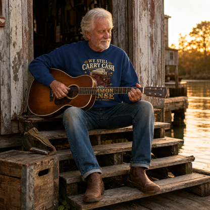 Senior man wearing navy vintage sweatshirt with printed cash and common sense slogan, playing guitar.