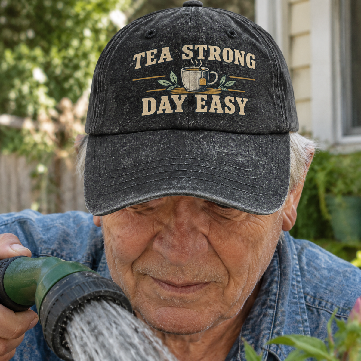 Black vintage washed cap with printed Tea Strong Day Easy slogan worn by senior gardener
