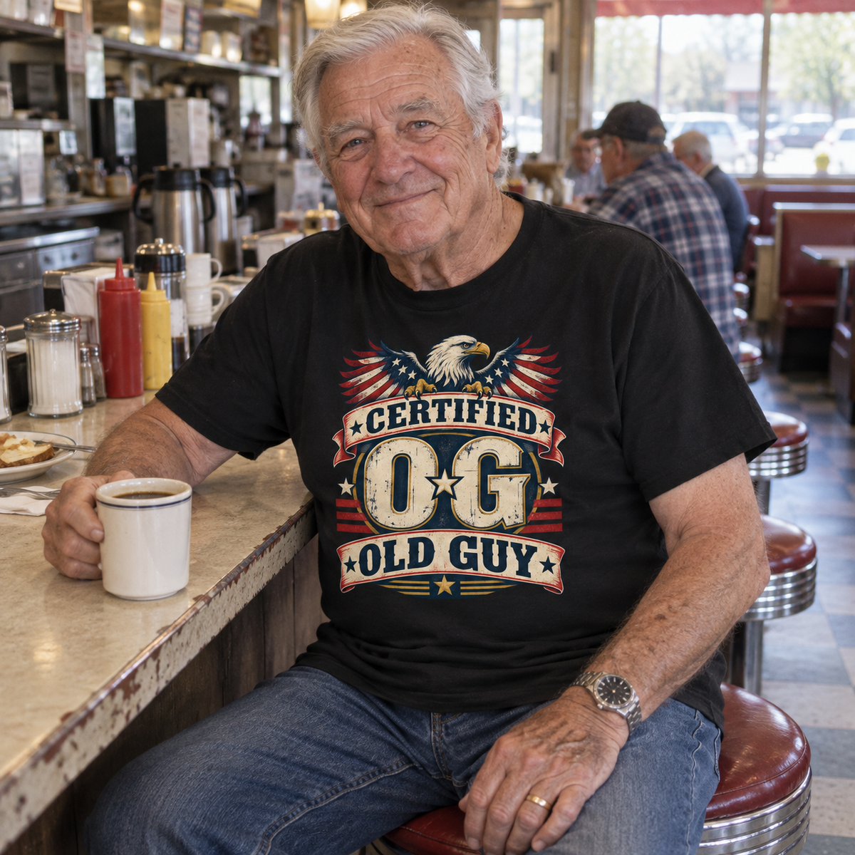 Senior man at diner wears black vintage t-shirt printed Certified OG Old Guy.