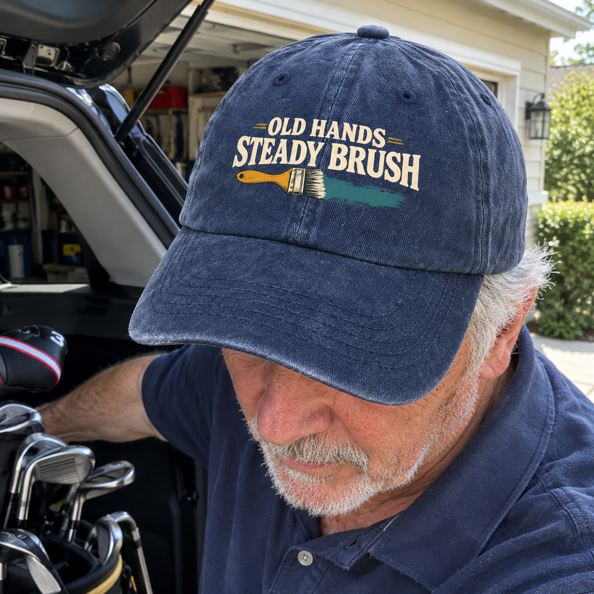Senior man wearing a navy vintage washed cap with printed “Old Hands = Steady Brush” slogan, lifestyle close-up.