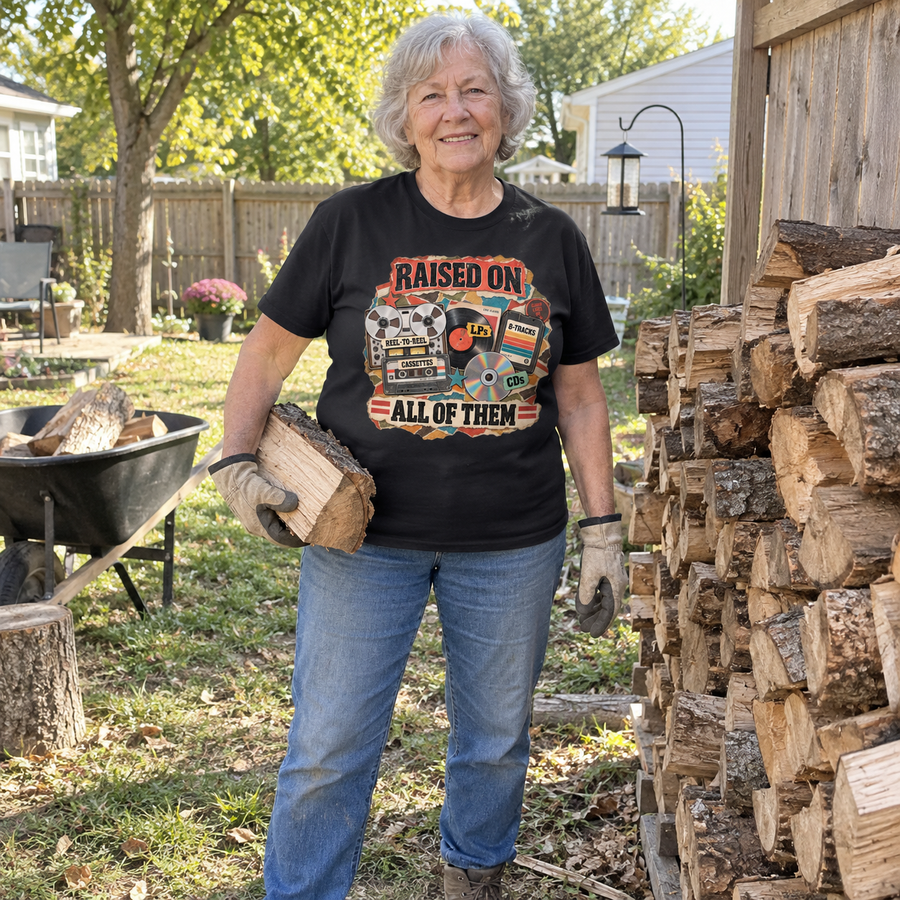 Senior woman holds firewood outdoors in black vintage t-shirt printed Raised On All Of Them.