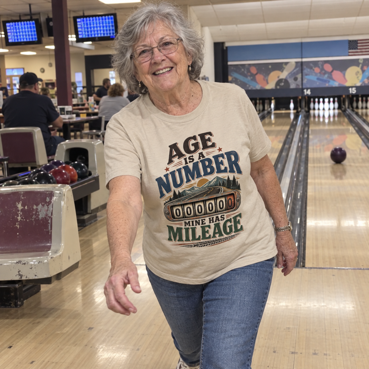 Senior woman at bowling alley wears beige vintage t-shirt printed Age Is A Number Mine Has Mileage