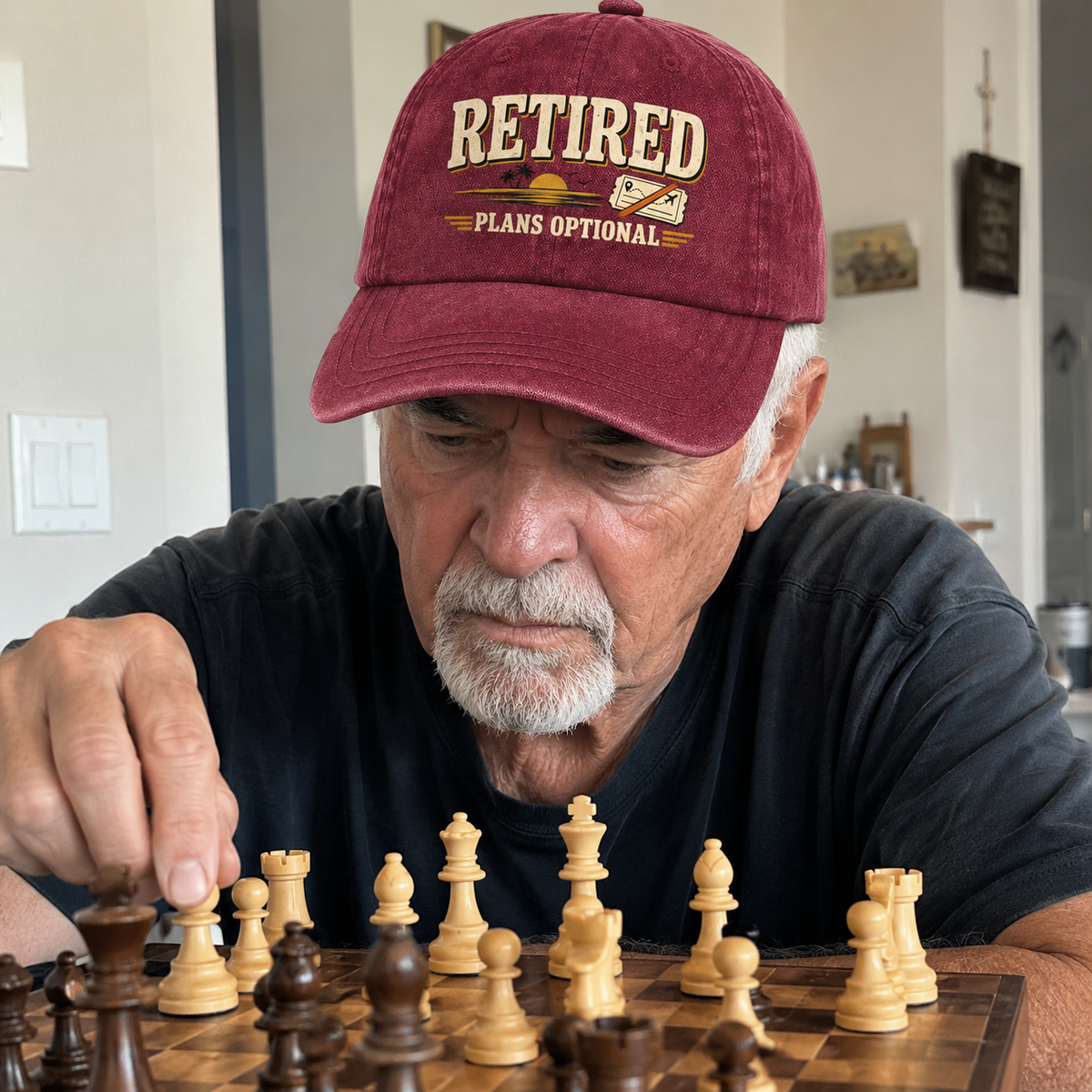 Senior man wearing burgundy vintage washed cap with printed Retired Plans Optional while playing chess