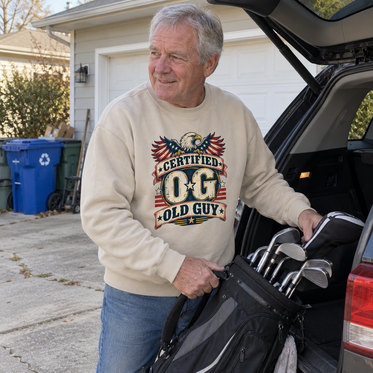 Senior man in cream vintage sweatshirt with printed Certified OG Old Guy beside golf clubs.
