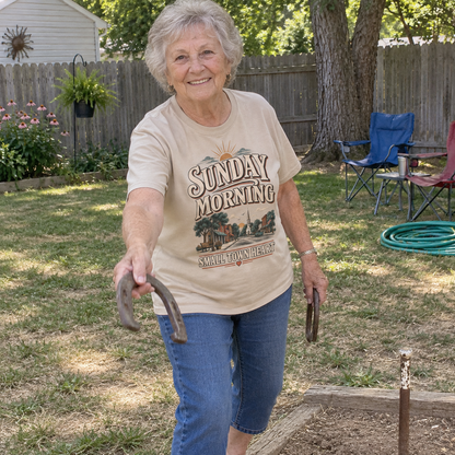 Senior woman plays horseshoes wearing beige vintage t-shirt printed Sunday Morning Small Town Heart