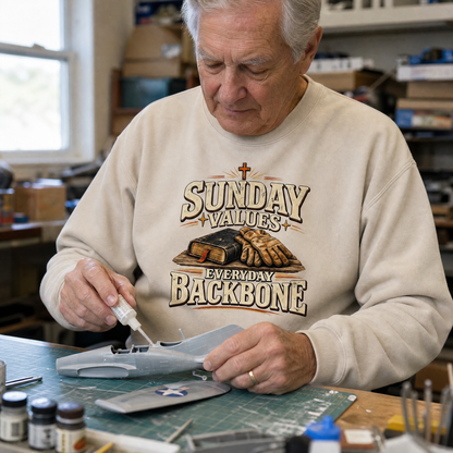 Senior man wearing a beige vintage sweatshirt with printed Sunday Values Everyday Backbone design, crafting model plane