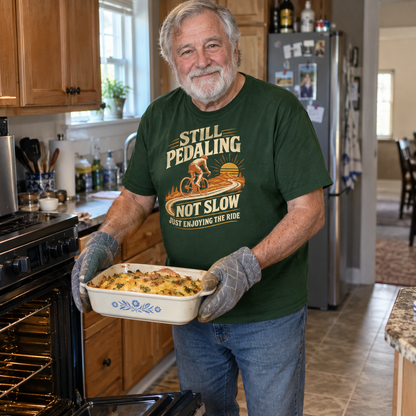Senior man wearing green vintage t-shirt with printed cycling slogan holds baked dish in kitchen