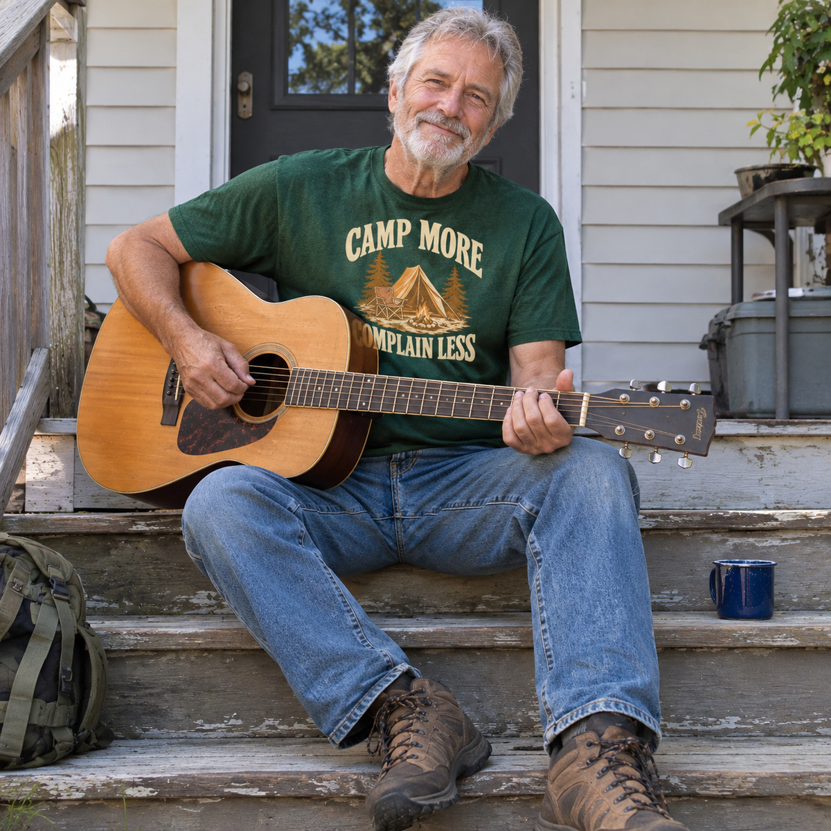 Senior man wearing green vintage t-shirt printed Camp More Complain Less, playing guitar outdoors.