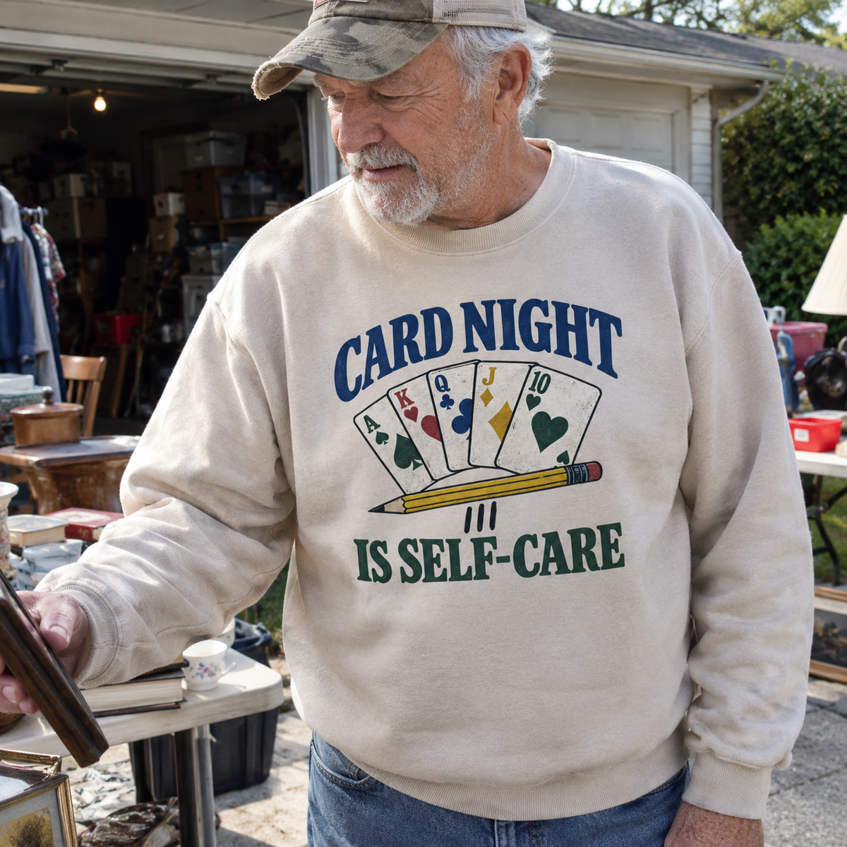 Senior man wearing beige vintage sweatshirt with printed Card Night Is Self-Care design outdoors.