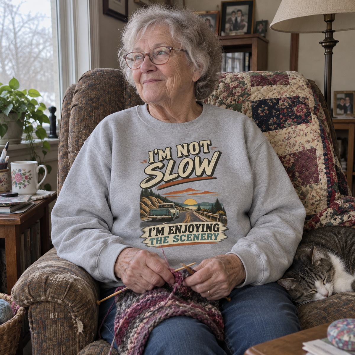 Senior woman knitting beside cat in gray vintage sweatshirt with printed road design
