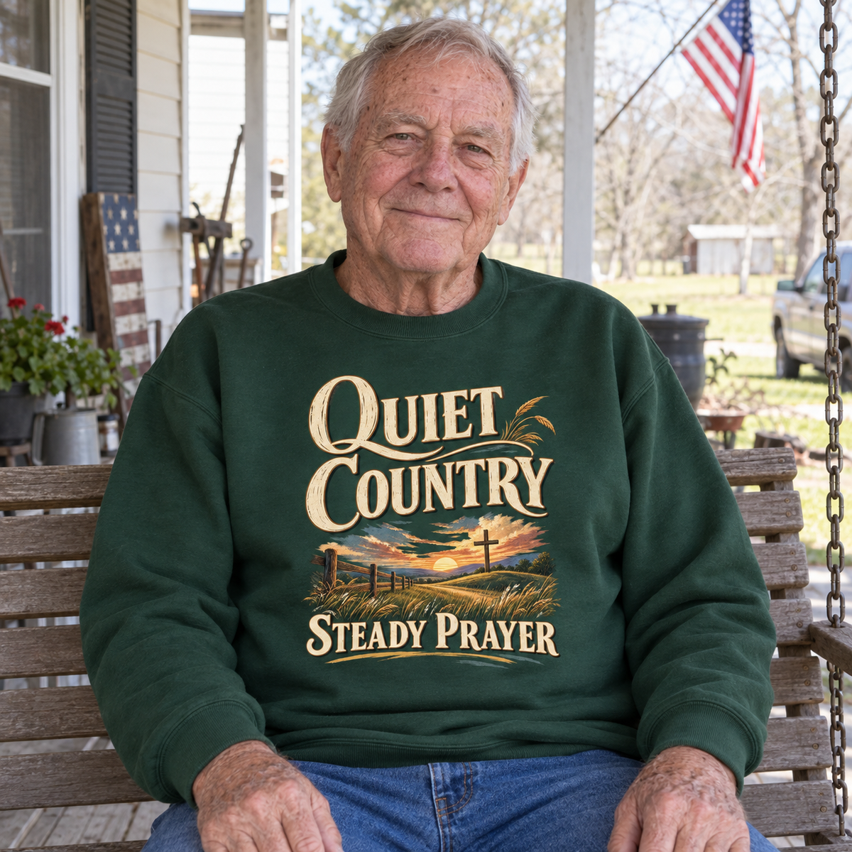 Senior man seated on porch wearing green vintage sweatshirt printed with Quiet Country Steady Prayer