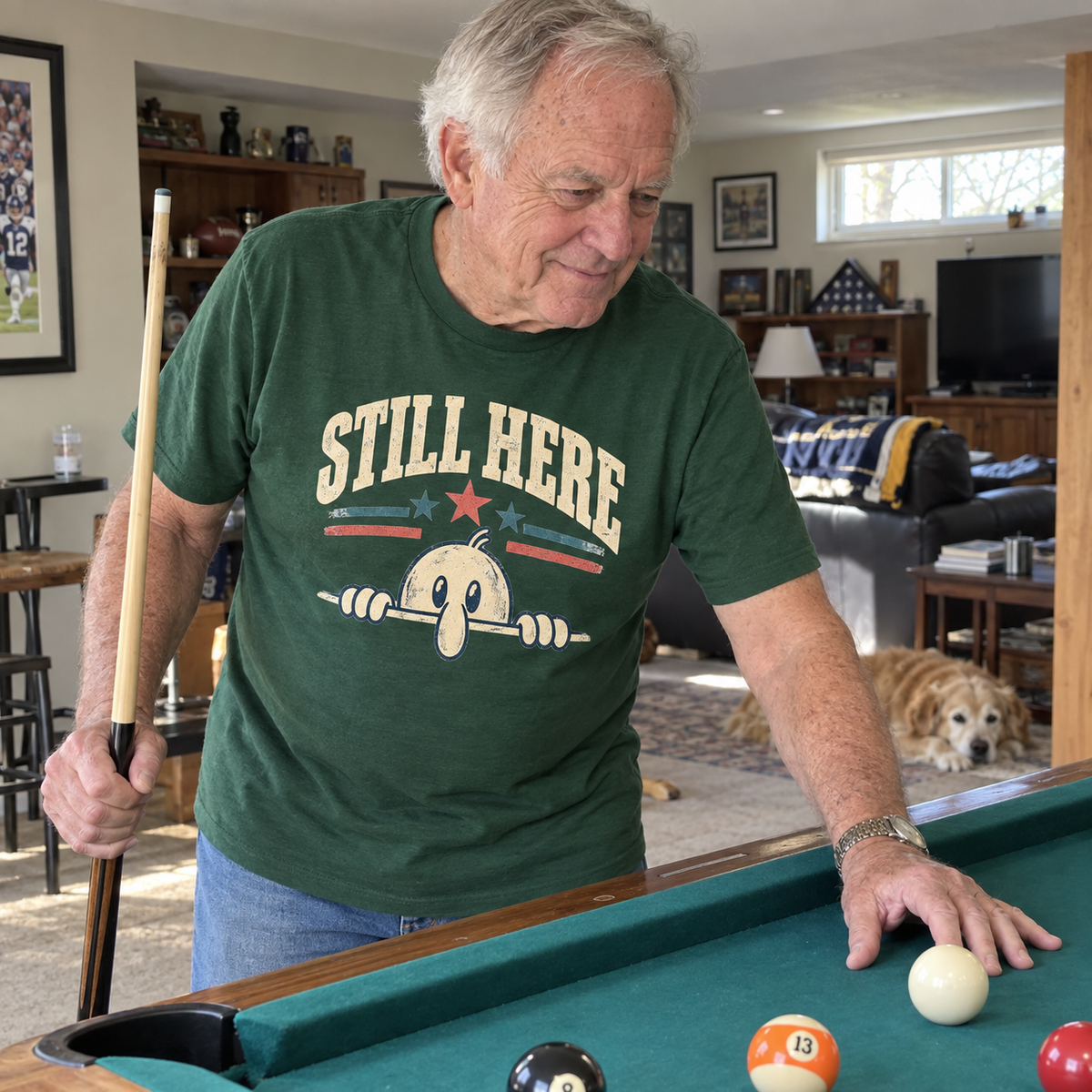 Senior man wearing green vintage t-shirt with printed Still Here design while playing pool.