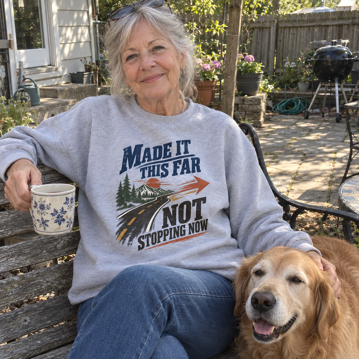 Senior woman outdoors wearing gray vintage sweatshirt with printed road and slogan beside dog
