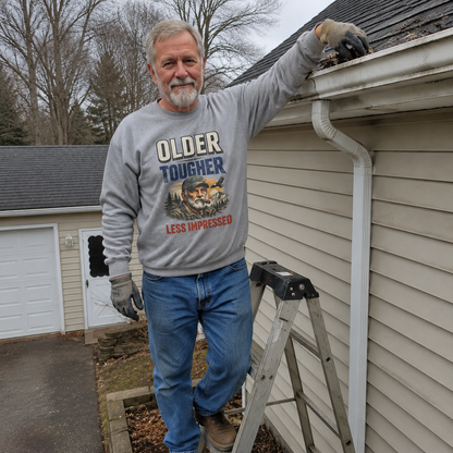 Gray vintage sweatshirt with printed “Older Tougher Less Impressed” worn by older man outdoors.