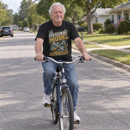 Senior man rides bicycle wearing black vintage t-shirt printed with Original Model Still In Service