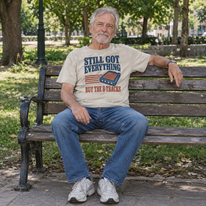 Senior man wears beige vintage t-shirt printed Still Got Everything But The 8-Tracks, seated outdoors.