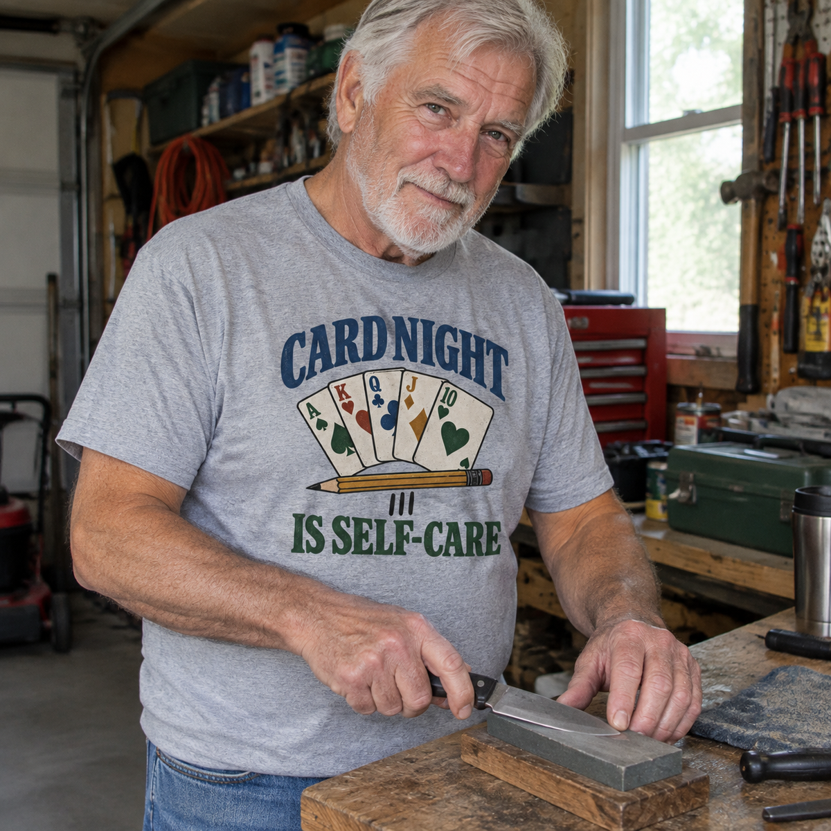 Senior man wearing gray vintage t-shirt with printed Card Night Is Self-Care design in workshop