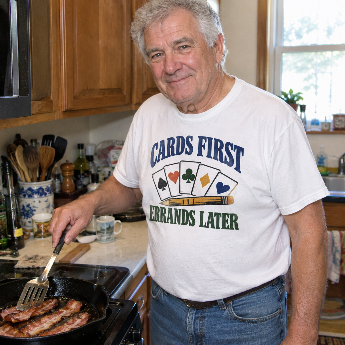 Senior man wearing white vintage t-shirt with printed Cards First. Errands Later slogan in kitchen lifestyle scene