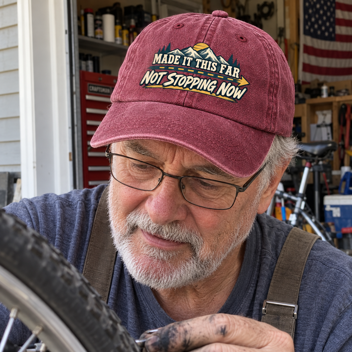 Senior man in garage wears burgundy vintage washed cap with printed mountain slogan.
