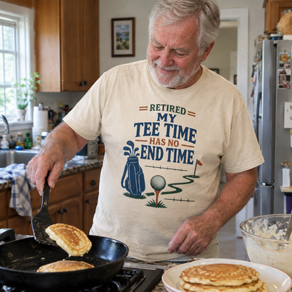 Senior man wearing cream vintage t-shirt with printed golf slogan while cooking pancakes.