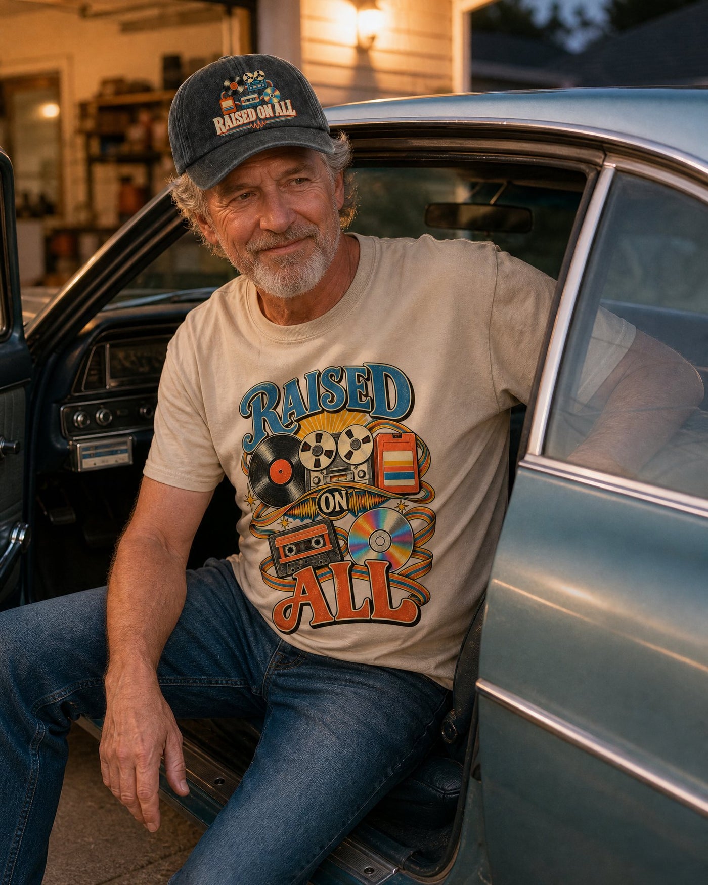 Man in the Raised On All sand tee and black cap sitting in his parked car with the door open