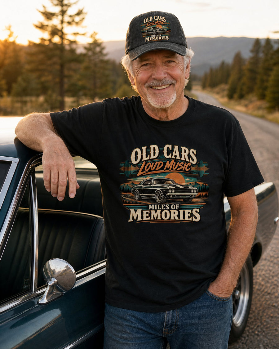 Man in the Old Cars Loud Music black tee and black cap leaning on the open door of his classic car on a country road